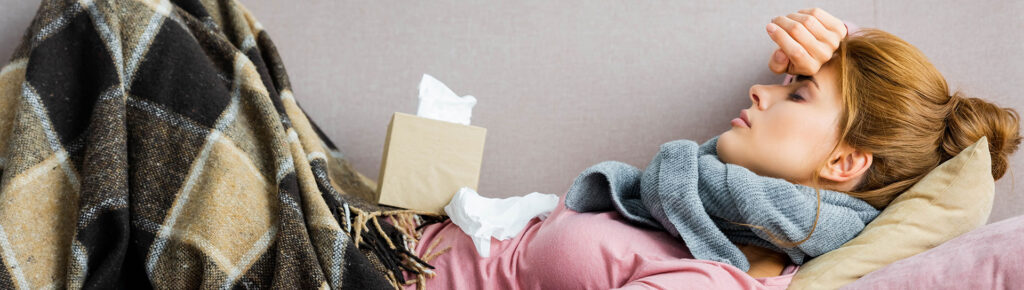 young woman laying down with hand over forehead and box of tissues on her lap