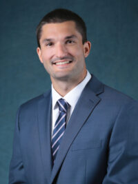 Douglas Rossi Headshot wearing blue suit and blue and pink striped tie